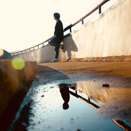 גבר בודד יושב על קצה גשר בטון בזמן שקיעה, משקיף על הנוף הרחוק ומהרהר בבדידות שאחרי הגירושין ופחד מאינטימיות בפרק ב'. בחזית שלולית מים המציגה השתקפות של המבנה והאדם.