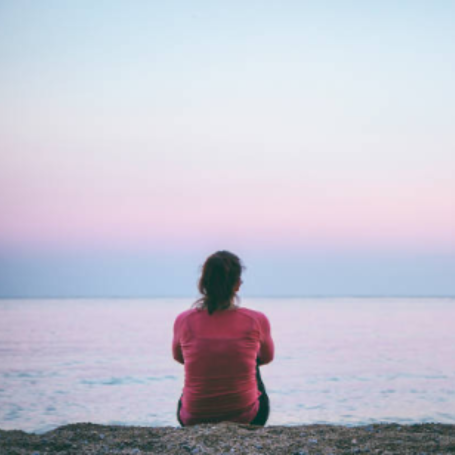 אישה יושבת לבד מול הים הרגוע, מסמלת תהליך ריפוי, מציאת שלווה והשתחררות מזיכרון פוסט-טראומטי בגירושין ומערכת יחסים רעילה.