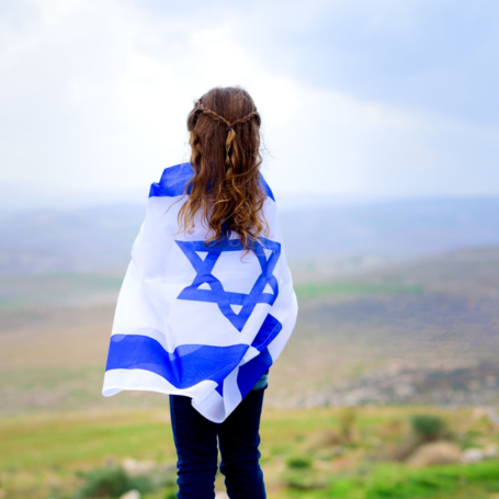 ילדה עטופה בדגל ישראל משקיפה אל האופק הפתוח ביום העצמאות, מסמלת מבט קדימה, תקווה ויציאה לדרך חדשה של עצמאות אישית ורגשית אחרי גירושין.