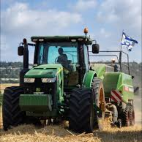 צילום אווירי של טרקטור חקלאי ירוק גורר עגלה ואוסף יבול בשדה. התמונה מסמלת את עונת הקטיף והקציר המזוהה עם חג השבועות ואווירת החג החקלאית.